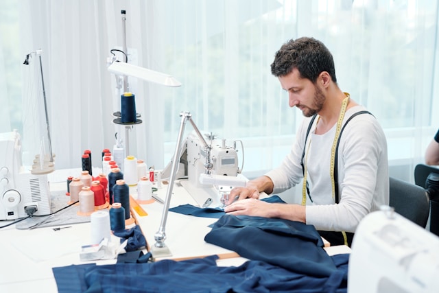 young-man-concentrating-on-sewing-clothing-item-on-machine-while-working-over-order