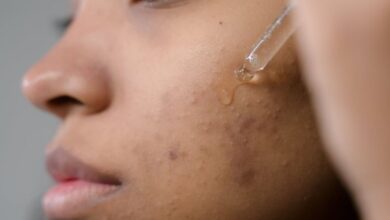 Acne Treatments - Close-up side view of a woman applying serum to her skin in a studio setting.