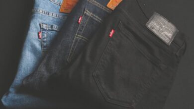 Pants - A stack of blue, dark, and black denim jeans folded on a dark surface.