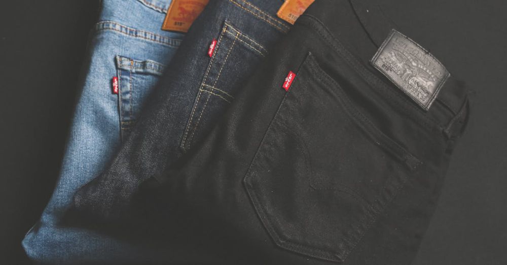 Pants - A stack of blue, dark, and black denim jeans folded on a dark surface.