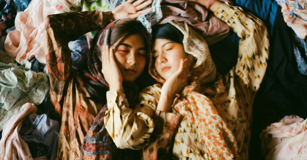 Scarves - Two women peacefully resting amidst vibrant fabrics, showcasing multicultural harmony and artistic expression.