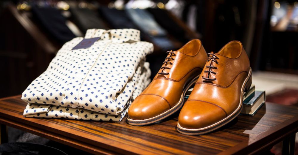 Men's Fashion - Elegant brown leather shoes and printed shirt displayed on a wooden table in a stylish clothing store.