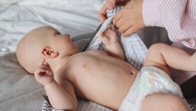 Diapers - Mother gently dresses infant on bed, showcasing tenderness and care.