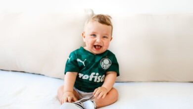 Baby Brands - Cute baby smiling while sitting on a sofa wearing a green sports jersey indoors.