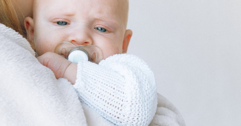 Baby Swaddles - Side view of casual female giving love and hug to cute newborn baby in knitted clothes while standing together in bedroom