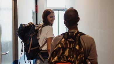 Hiking Backpacks - Two young travelers with backpacks leaving a hostel through a narrow corridor.