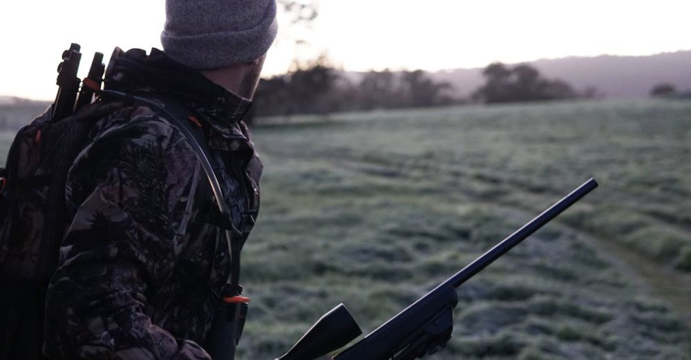 Hunting Gear - Camouflaged hunter surveying the landscape with rifle at dawn in Victoria, Australia.