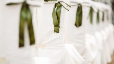 Seat Covers - White chairs adorned with green ribbon bows, perfect for a wedding or elegant event setup.