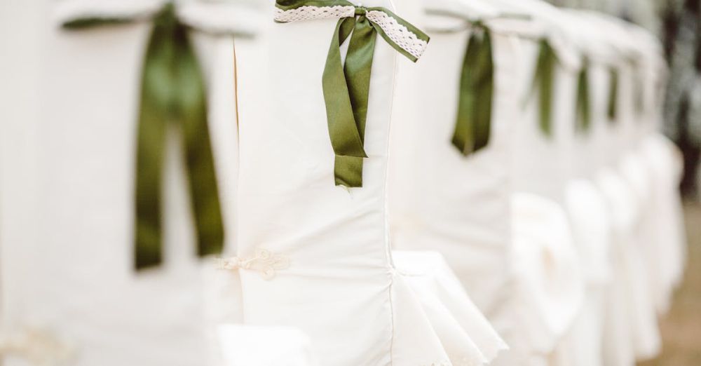 Seat Covers - White chairs adorned with green ribbon bows, perfect for a wedding or elegant event setup.