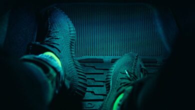 Car Mats - Dark interior of a car with feet in sneakers illuminated by neon light, creating a moody atmosphere.