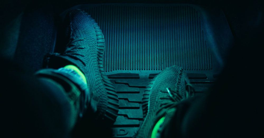 Car Mats - Dark interior of a car with feet in sneakers illuminated by neon light, creating a moody atmosphere.