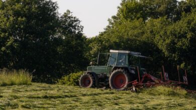 Tow Hitches - A tractor operates in a lush green field during summer, surrounded by trees.