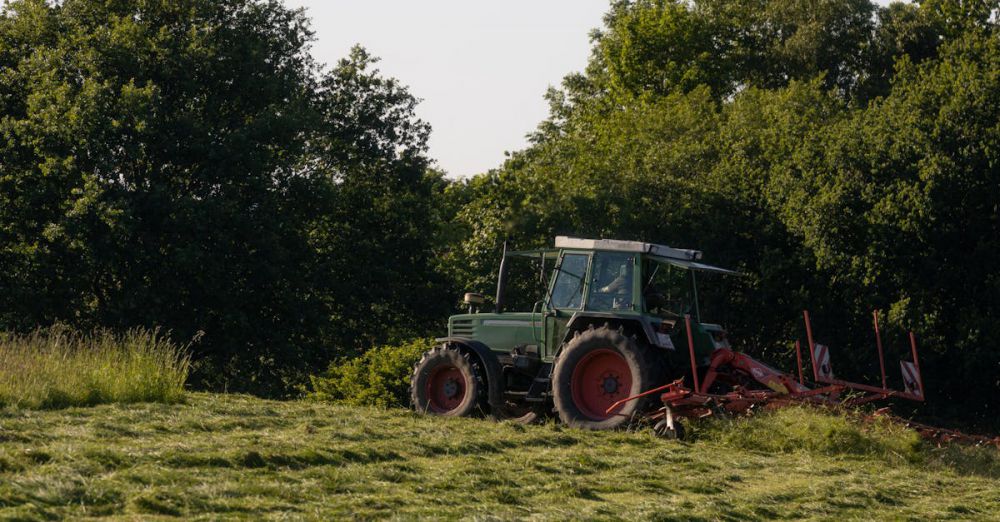 Tow Hitches - A tractor operates in a lush green field during summer, surrounded by trees.