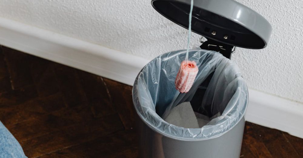 Floor Liners - Person disposing of a tampon into a foot-pedal trash can indoors.