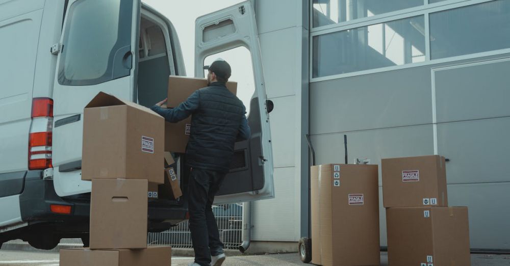 Cargo Boxes - A delivery man unloading cardboard boxes from a van at a warehouse during the day.