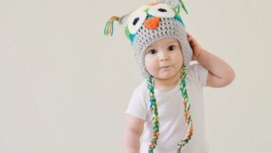 Baby Products - A cute baby wearing an owl hat standing in a basket, smiling and playful.