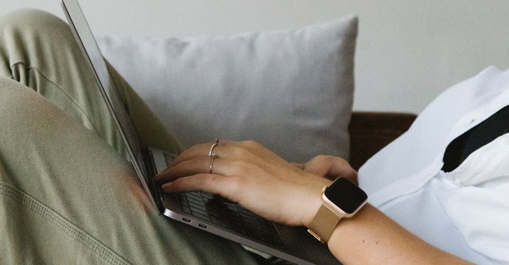 Smart Home Gadgets - Side view of crop unrecognizable female freelancer in casual clothes and smartwatch lying on comfortable sofa and working remotely on laptop