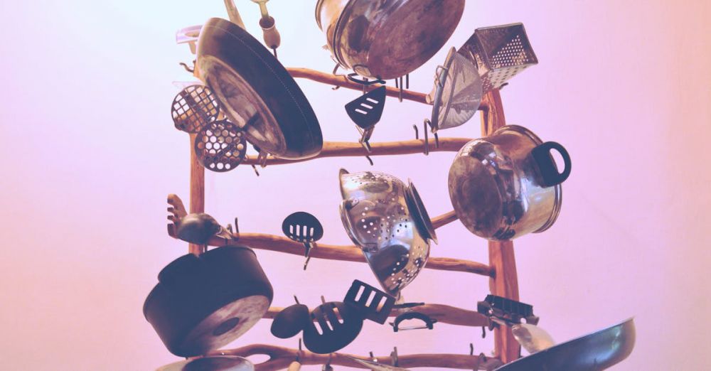 Cookware - Artistic assortment of hanging kitchen cookware and utensils on a wooden rack indoors.