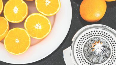 Juicer - Top view of fresh oranges sliced on a white plate with a metal juicer nearby.