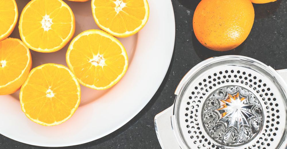 Juicer - Top view of fresh oranges sliced on a white plate with a metal juicer nearby.