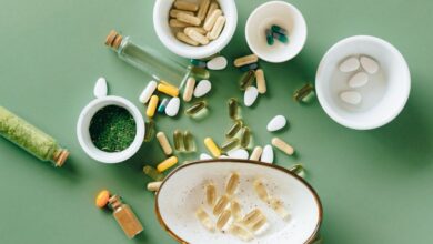 Health Supplements - Top view of various herbal and pharmaceutical supplements in ceramic bowls on a green background.