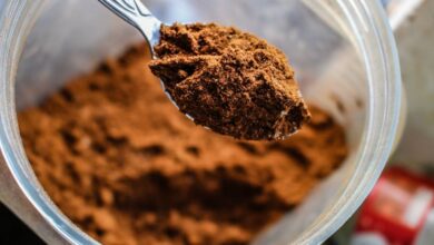 Protein Powder - Focused shot of a spoon scooping cocoa powder from a container, emphasizing texture.