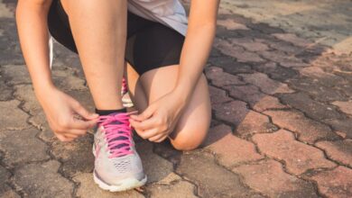 Running Shoes - Adult woman tying pink laces on running shoes outdoors. Focuses on fitness and lifestyle.