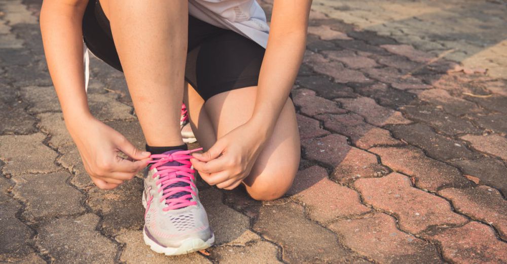 Running Shoes - Adult woman tying pink laces on running shoes outdoors. Focuses on fitness and lifestyle.