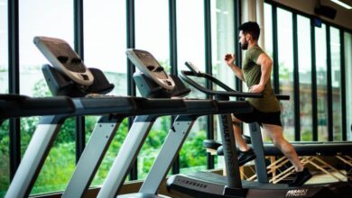 Treadmill - Young man workouts on treadmill in modern gym with large windows and natural light.