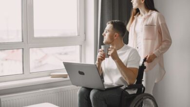 Home Health Devices - Man in wheelchair with laptop and coffee, gazing out window with a woman beside him.