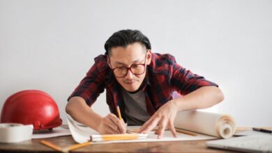 Smart Helmets - Inspired young male engineer in glasses drawing draft on paper bending over table against white wall