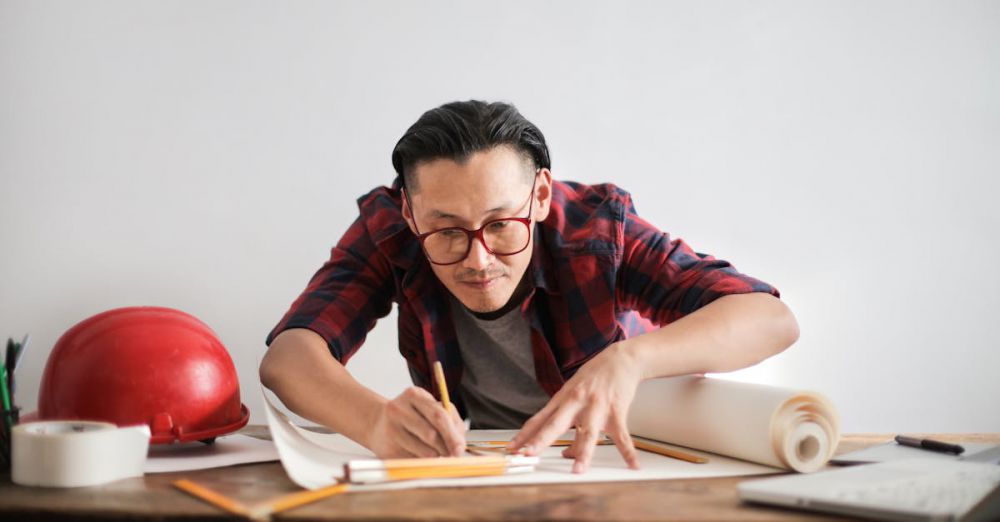 Smart Helmets - Inspired young male engineer in glasses drawing draft on paper bending over table against white wall