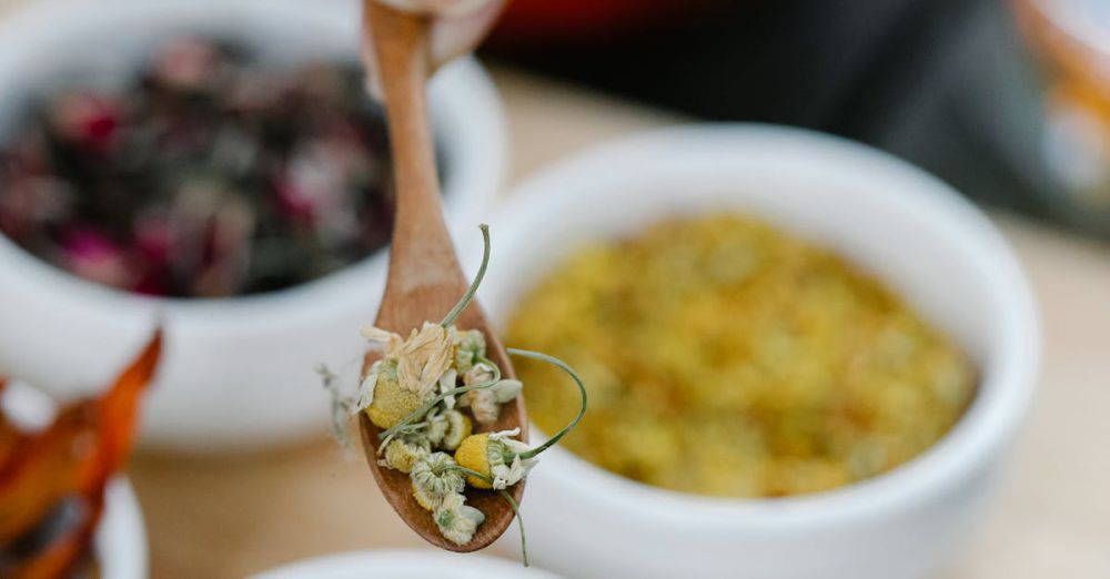 Wooden Bowls - Close-up of a hand holding a wooden spoon with dried herbs and flowers in bowls.