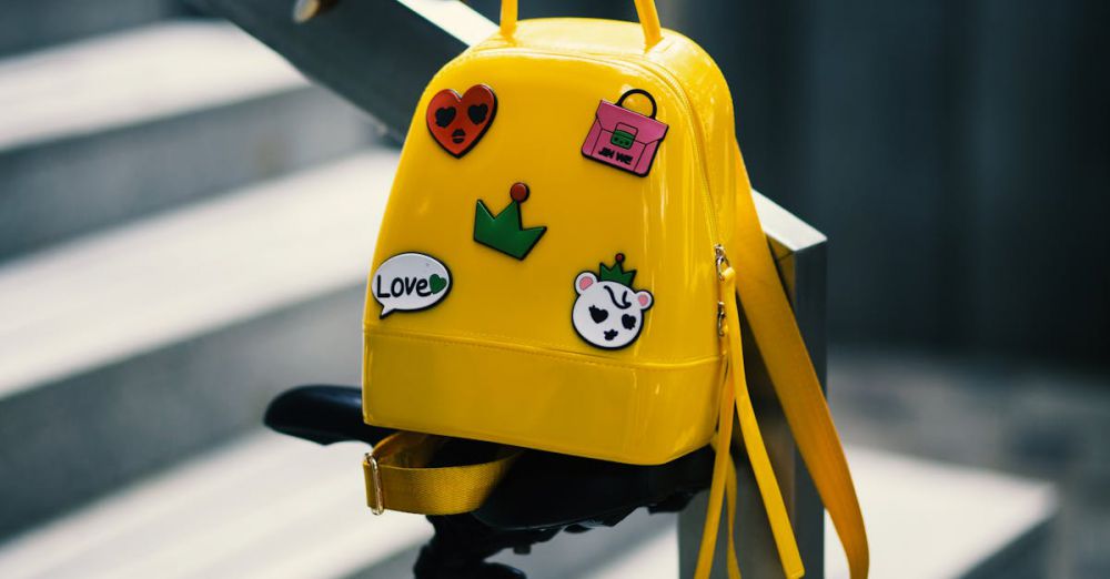 Bags - Stylish yellow backpack with playful stickers on a bicycle saddle outdoors.