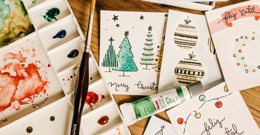 Greeting Cards - Artistic holiday card designs with watercolor paints and brushes on a wooden table.