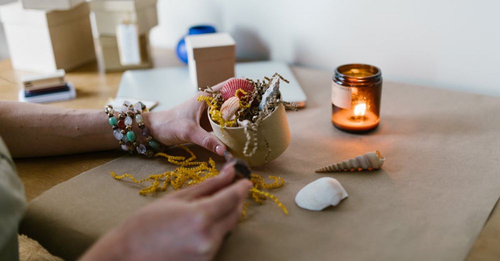 Jewelry Boxes - Hand arranging seashells on craft paper with a lit scented candle in calm, creative setting.