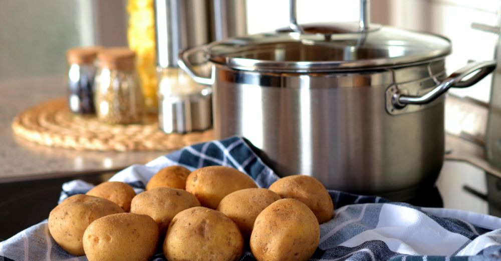 Cookware - Fresh potatoes on cloth beside a stainless pot, ready for cooking in a modern kitchen.