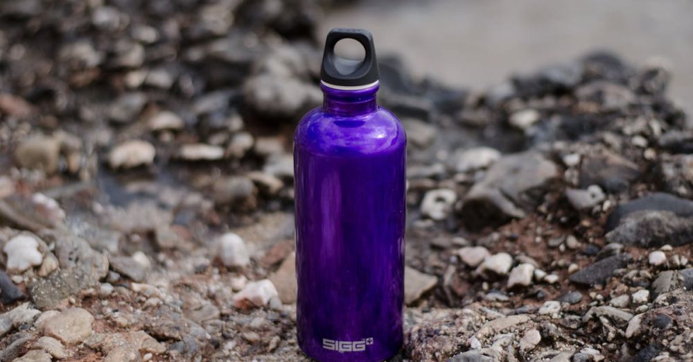 Water Bottles - Close-up of a purple water bottle on rocky ground, perfect for outdoor adventures.