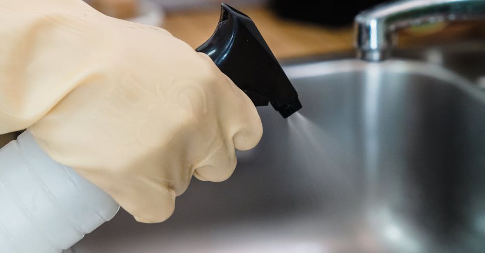 Cleaning Products - Close-up of a gloved hand cleaning a kitchen sink using a spray bottle, showcasing hygiene.