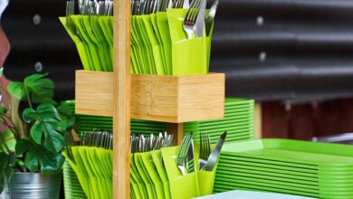 Cutlery Sets - A bamboo cutlery holder with green napkins and plants on a wooden counter.