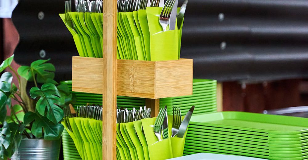 Cutlery Sets - A bamboo cutlery holder with green napkins and plants on a wooden counter.