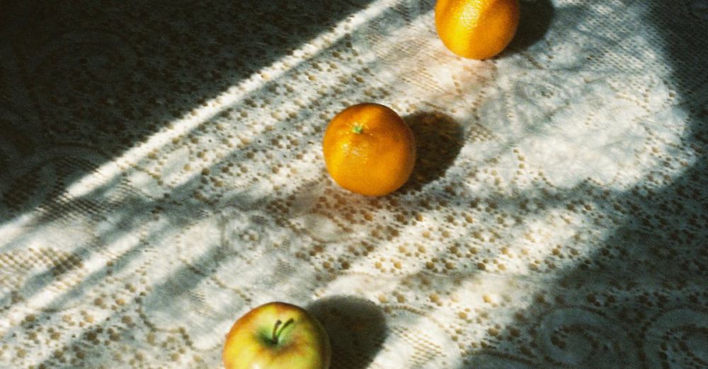 Heat Packs - A minimalist composition featuring oranges and an apple under morning light on a textured tablecloth.