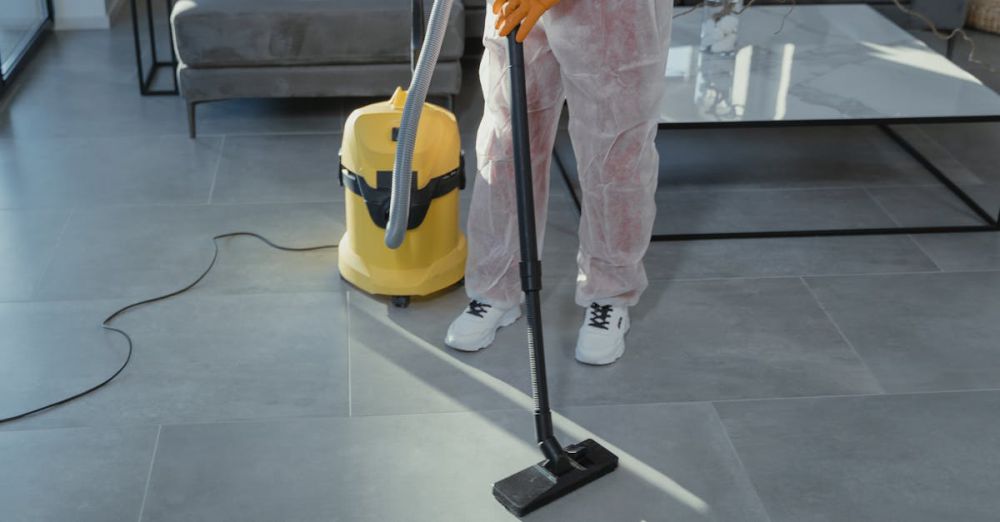 Cleaning Tools - A professional cleaner in protective gear vacuuming the floor in a modern living room.