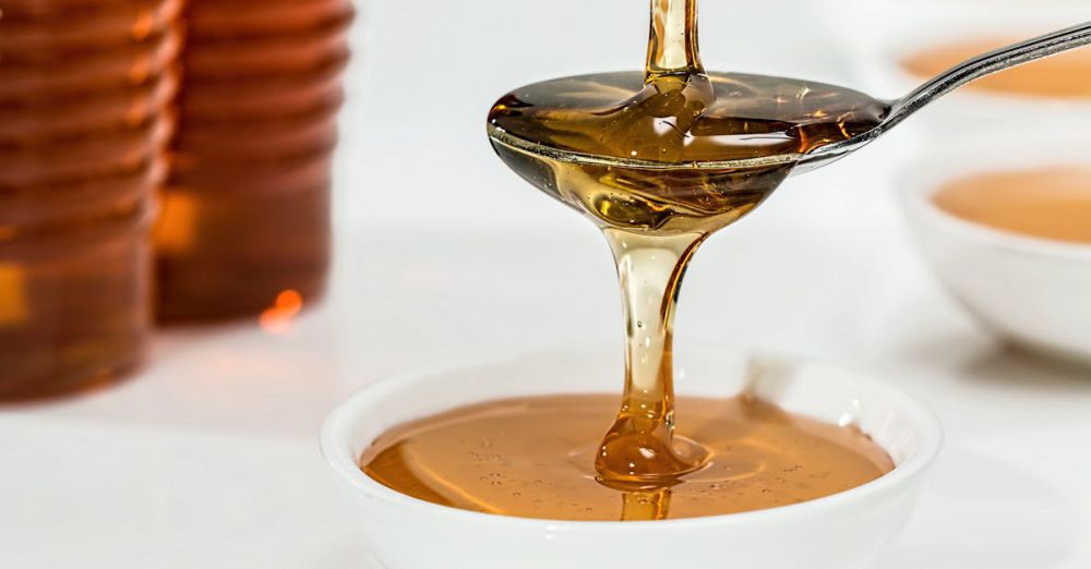 Syrup - Delicious honey pouring slowly from a spoon into a white bowl, highlighting its golden hue and viscosity.