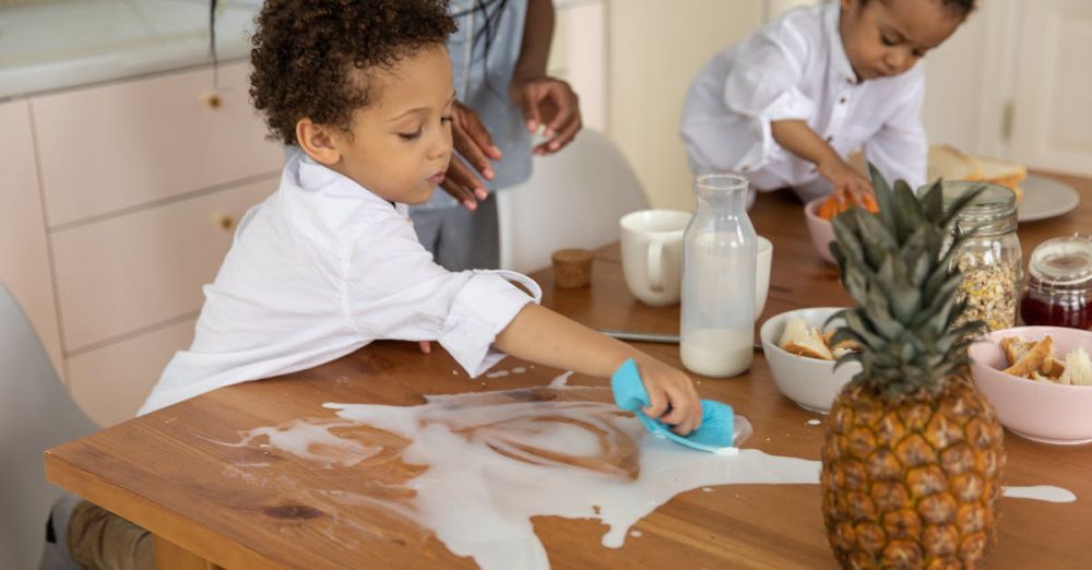 Kitchen Sponges - Children clean up a milk spill on a wooden breakfast table with family nearby, creating a cute and lively morning scene.