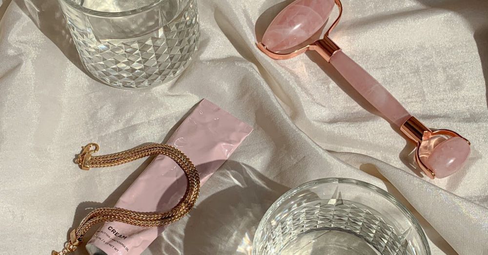 Sleep Products - Flat lay of beauty items with rose quartz roller and glass on a satin sheet, emphasizing self-care.