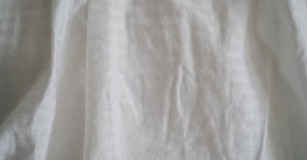 Silk Pillowcases - Detailed close-up of wrinkled white cotton fabric texture, showcasing textile patterns and folds.