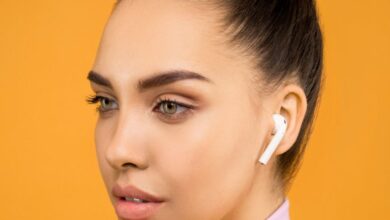 Earbuds - Young woman wearing earbuds, posing against a vibrant orange background. Fashionable and modern.