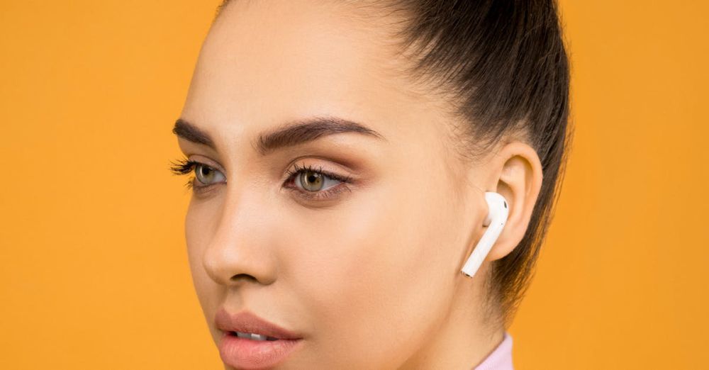 Earbuds - Young woman wearing earbuds, posing against a vibrant orange background. Fashionable and modern.