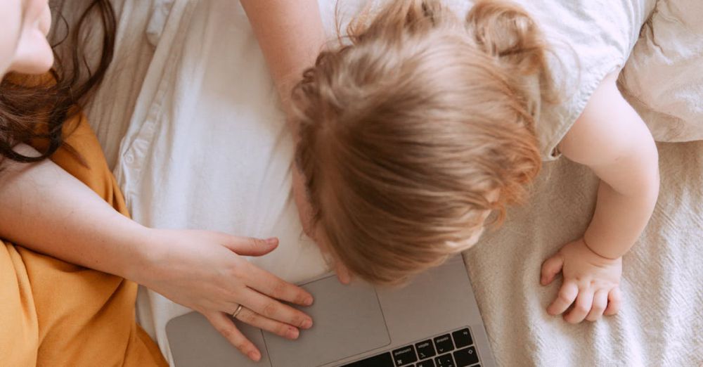 Kids Gadgets - A mother and child comfortably using a laptop on a cozy bed, enjoying shared screen time.